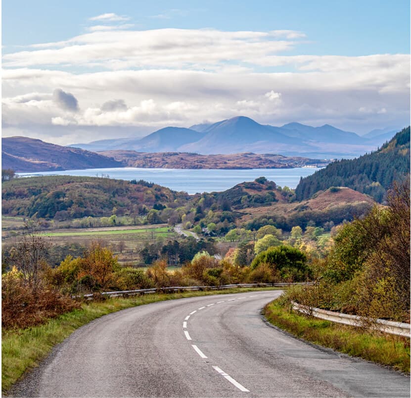 Highland road winding through autumn hills with distant mountains