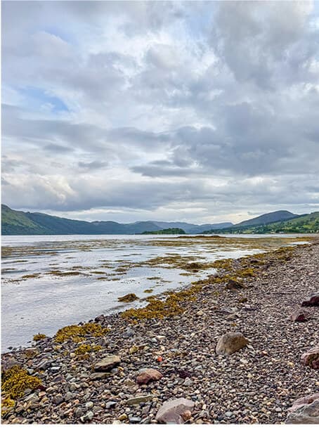Pebble shore of a Highland loch under cloudy skies