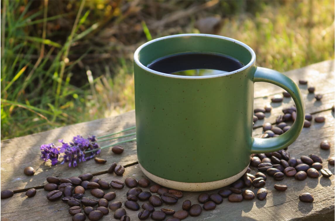Green mug of black coffee on a wooden bench with coffee beans scattered around